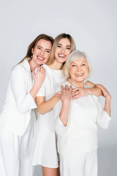Tre generazioni di donne sorridenti che guardano la macchina fotografica e si abbracciano isolate sul grigio — Foto stock