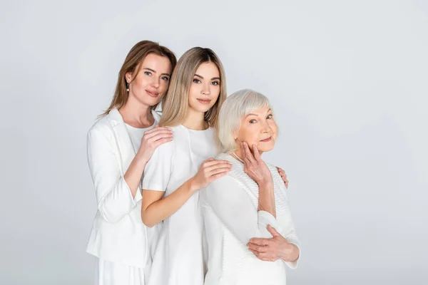 Tre generazioni di donne gioiose sorridenti guardando la macchina fotografica e abbracciandosi isolate sul grigio — Foto stock