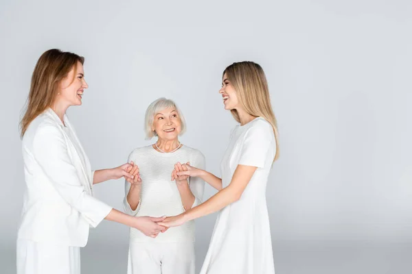 Tres generaciones de mujeres felices sonriendo mientras se toman de las manos aisladas en gris - foto de stock