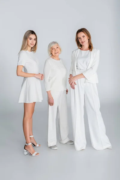Longitud completa de tres generaciones de mujeres felices sonriendo mientras están de pie en gris - foto de stock