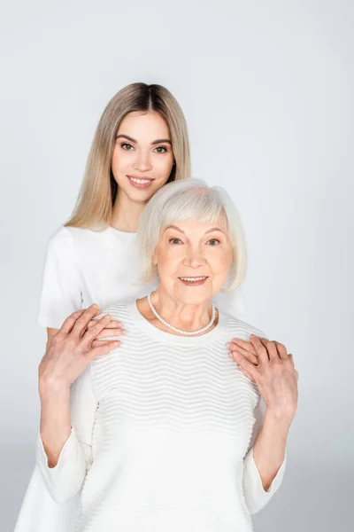 Allegra nipote abbracciando la nonna anziana isolata su grigio — Foto stock