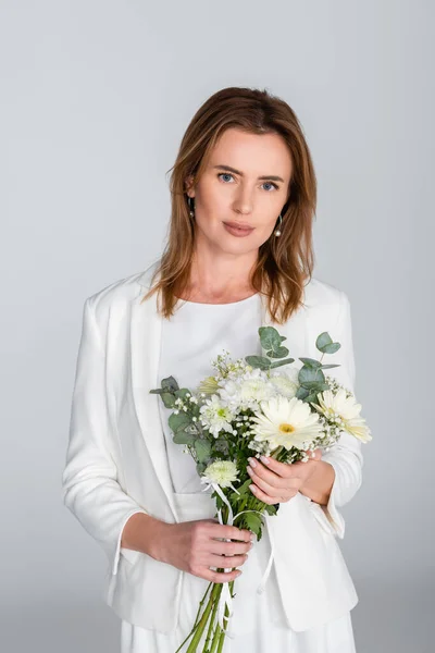 Woman holding bouquet of flowers and looking at camera isolated on grey — Stock Photo