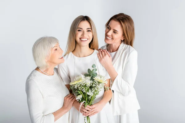 Fröhliche junge Frau lächelt, während sie Blumen in der Nähe von Mutter und Oma hält, isoliert auf grau — Stockfoto