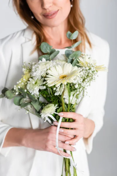 Cropped view of woman holding bouquet of flowers and looking at camera isolated on grey — Stock Photo