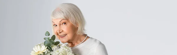 Felice donna anziana con i capelli grigi che tiene i fiori isolati su grigio, banner — Foto stock