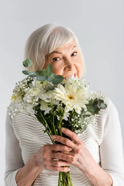 Mujer jubilada con pelo gris sosteniendo flores aisladas en gris - foto de stock