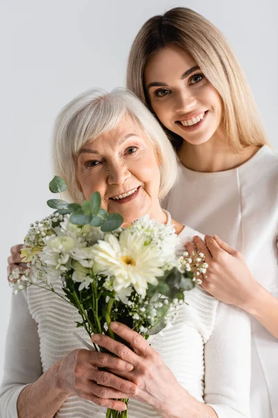 Glücklich junge Frau lächelt neben Oma mit Blumen isoliert auf grau — Stockfoto