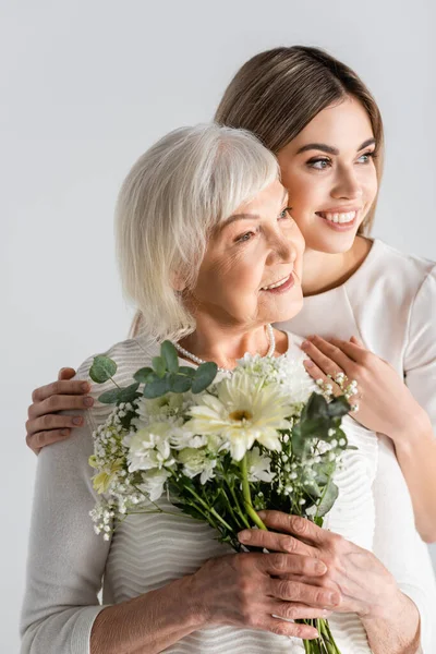 Allegra giovane donna sorridente con nonna che tiene fiori isolati sul grigio — Foto stock