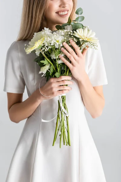 Abgeschnittene Ansicht einer jungen Frau, die lächelt, während sie Blumen isoliert auf grau hält — Stockfoto