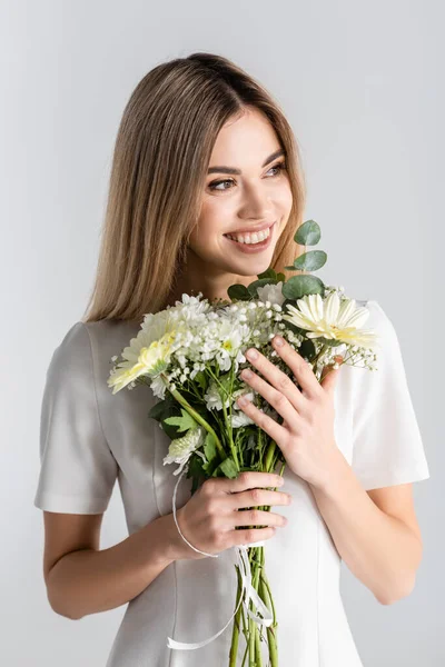 Glückliche junge Frau lächelt, während sie Blumen in grau hält — Stockfoto