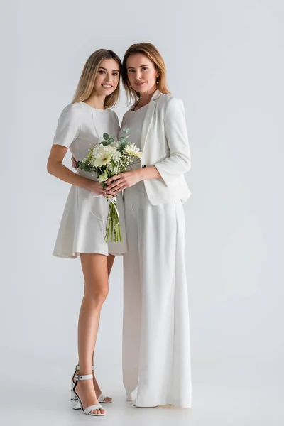 Pleine longueur de heureuse jeune fille et mère debout avec des fleurs sur gris — Photo de stock