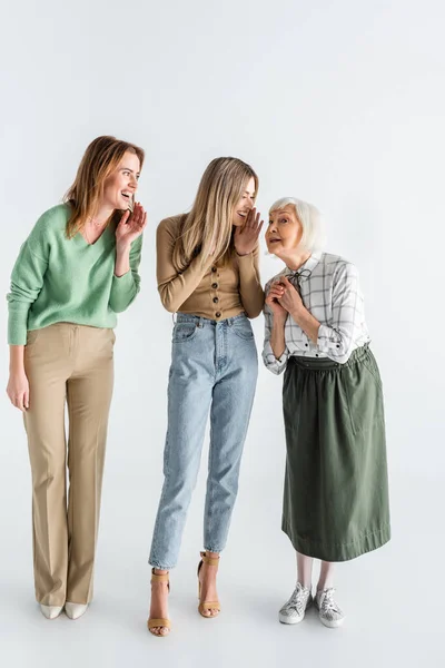 Pleine longueur de trois générations de femmes heureuses souriant tout en bavardant sur le blanc — Photo de stock