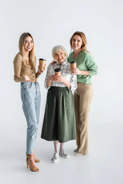 Full length of three generation of happy women holding paper cups on white — Stock Photo