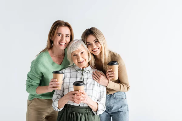 Tres generaciones de mujeres felices sosteniendo vasos de papel aislados en blanco - foto de stock