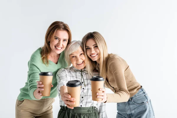 Three generation of happy women holding paper cups in outstretched hands isolated on white — Stock Photo