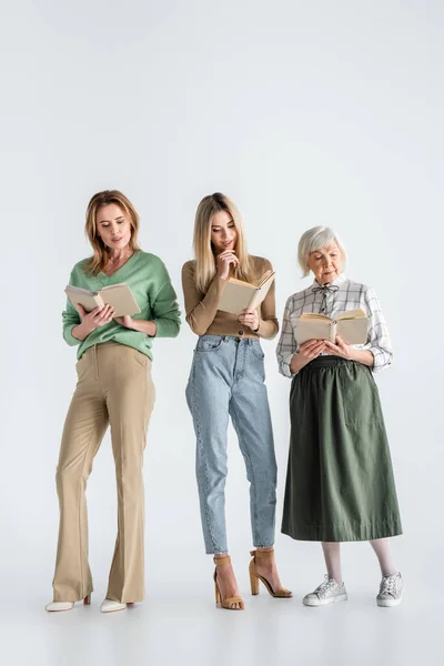 Longueur totale de trois générations de femmes lisant des livres sur le blanc — Photo de stock