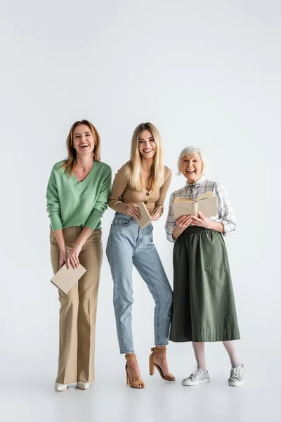 Pleine longueur de trois générations de femmes heureuses tenant des livres sur blanc — Photo de stock