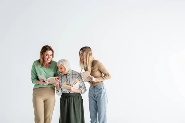 Tre generazioni di donne felici che tengono libri e sorridono isolate sul bianco — Foto stock