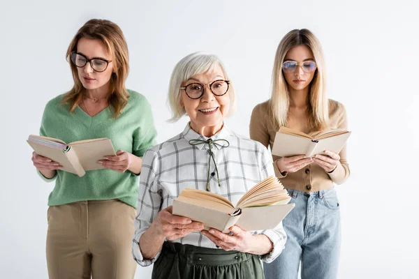 Trois générations de femmes heureuses dans des lunettes de lecture de livres isolés sur blanc — Photo de stock