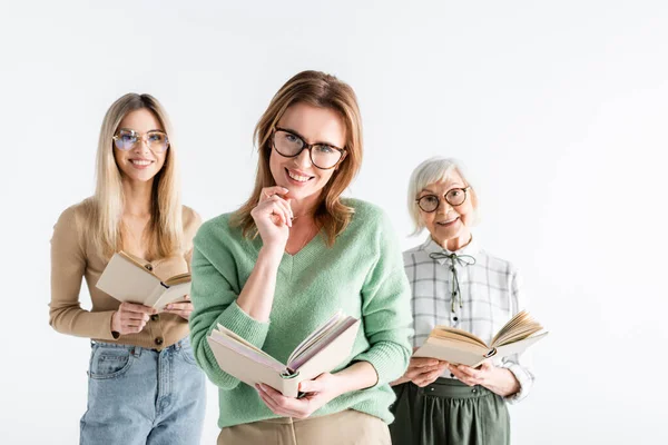 Trois générations de femmes souriantes dans des lunettes de lecture de livres isolés sur blanc — Photo de stock