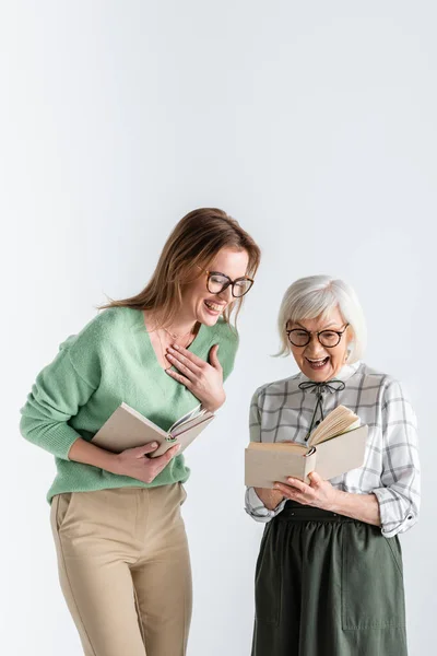 Seniorin lacht mit Tochter in Brille und hält Bücher isoliert auf weißem Papier — Stockfoto