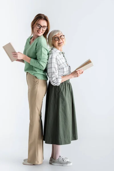 В полный рост пожилая женщина и дочь в очках с книгами на белом — стоковое фото