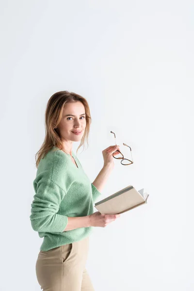 Mujer alegre sosteniendo gafas y libro aislado en blanco - foto de stock