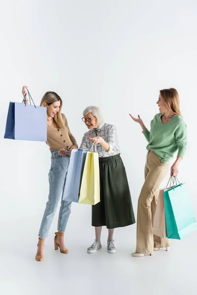 Longitud completa de tres generaciones de mujeres felices sosteniendo bolsas de compras en blanco - foto de stock