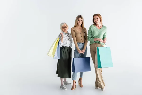 Full length of three generation of cheerful women holding shopping bags on white — Stock Photo