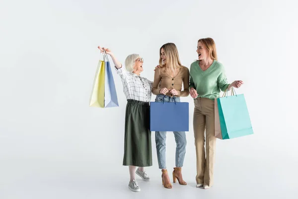 Piena lunghezza di tre generazioni di donne gioiose che tengono borse della spesa su bianco — Foto stock