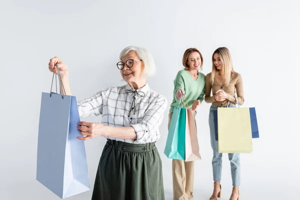 Feliz mulher sênior segurando sacos de compras perto de filha e neta no fundo borrado — Fotografia de Stock
