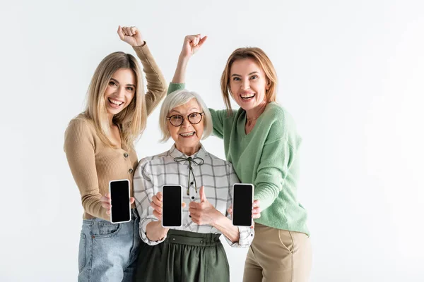 Tres generaciones de mujeres excitadas sosteniendo teléfonos inteligentes con pantalla en blanco aislada en blanco - foto de stock