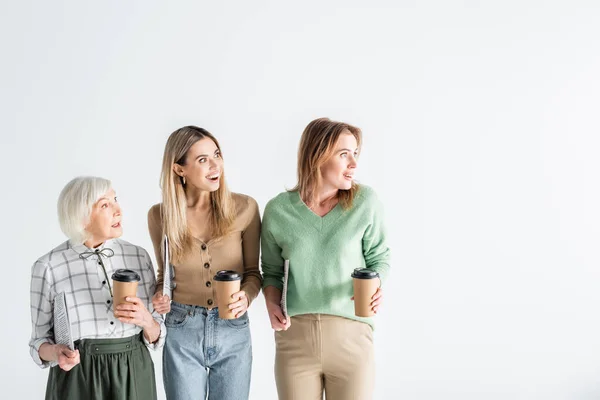 Tres generaciones de mujeres asombradas sosteniendo periódicos y vasos de papel aislados en blanco - foto de stock