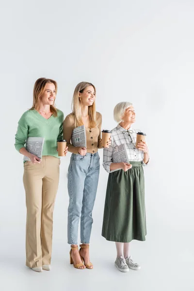 Drei Generationen glücklicher Frauen, die Zeitungen und Pappbecher auf weiß halten — Stockfoto