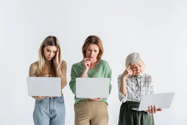 Três gerações de mulheres pensativas usando laptops isolados em branco — Fotografia de Stock