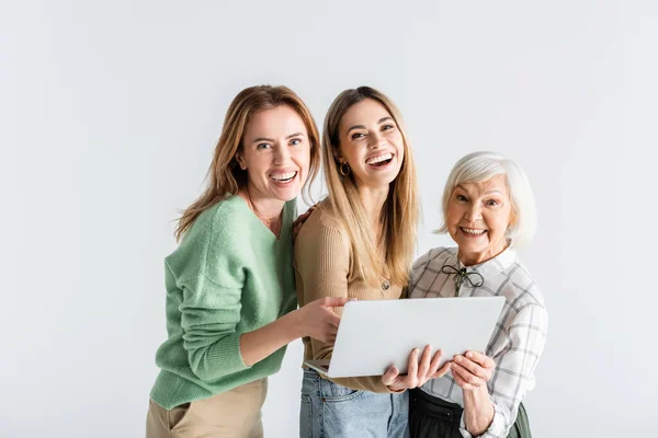 Trois générations de femmes heureuses regardant la caméra près d'un ordinateur portable isolé sur blanc — Photo de stock