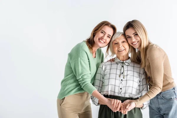 Três gerações de mulheres felizes olhando para a câmera e segurando as mãos isoladas no branco — Fotografia de Stock