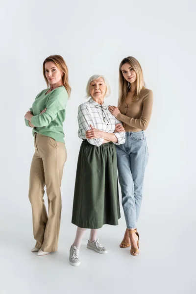 Longitud completa de tres generaciones de mujeres mirando a la cámara y posando en blanco - foto de stock