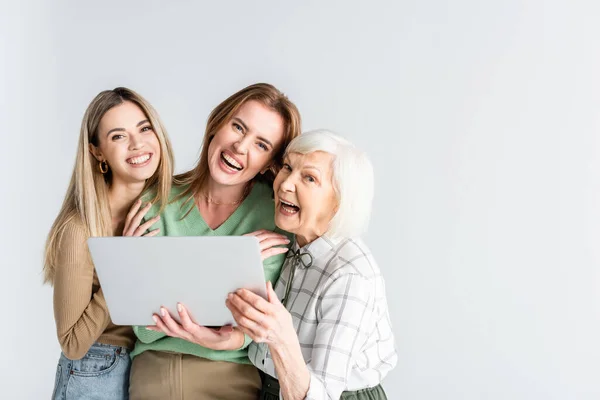 Tre generazioni di donne gioiose guardando la fotocamera vicino al computer portatile isolato su bianco — Foto stock