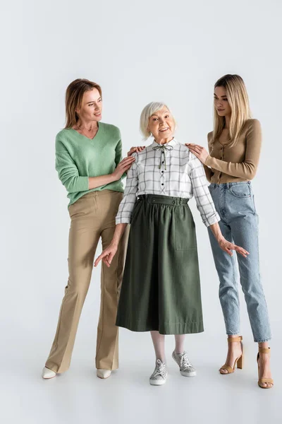 Full length of women looking at cheerful senior woman on white — Stock Photo