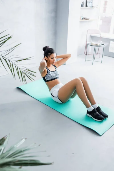 Junge Amerikanerin in Sportbekleidung beim Bauchmuskeltraining auf Fitnessmatte zu Hause, verschwommener Vordergrund — Stockfoto