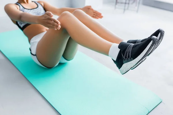 Ausgeschnittene Ansicht einer afrikanisch-amerikanischen Sportlerin beim Bauchmuskeltraining auf einer Fitnessmatte, verschwommener Hintergrund — Stockfoto