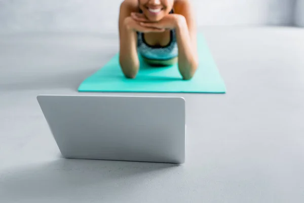 Selektiver Fokus des Laptops in der Nähe lächelnder afrikanisch-amerikanischer Sportlerin auf verschwommenem Hintergrund, abgeschnittene Ansicht — Stockfoto