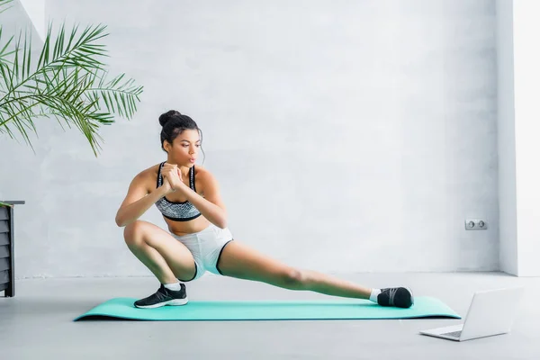 Young african american sportswoman doing stretching exercise on fitness man near laptop — Stock Photo