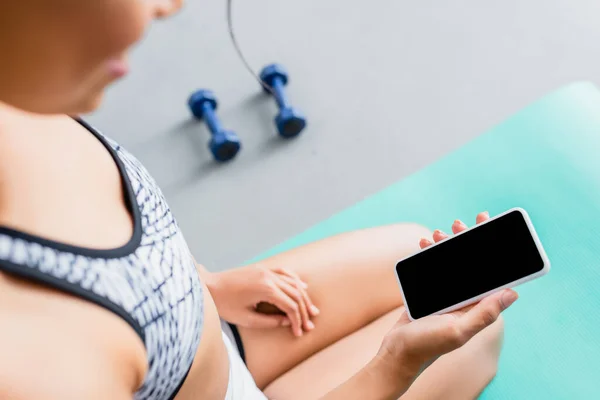 Partial view of african american sportswoman holding mobile phone with blank screen near dumbbells on blurred background — Stock Photo