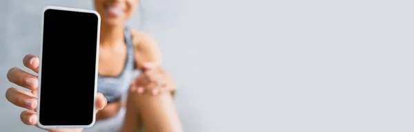 Cropped view of african american sportswoman showing smartphone with blank screen, blurred background, banner — Stock Photo