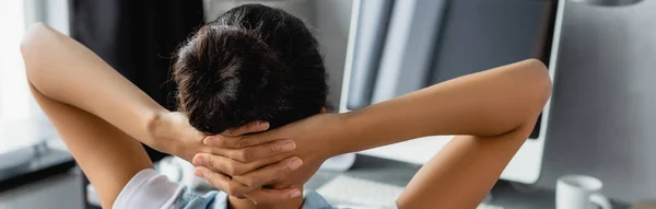 Rückansicht eines afrikanisch-amerikanischen Freelancers mit Händen hinter dem Kopf in der Nähe eines verschwommenen Monitors, Banner — Stockfoto