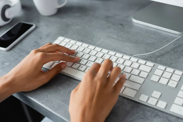 Partial view of african american freelancer typing on keyboard near smartphone with blank screen — Stock Photo