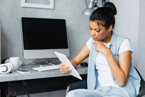 Pigiste afro-américain réfléchi utilisant une tablette numérique près de l'écran de l'ordinateur avec écran blanc — Photo de stock