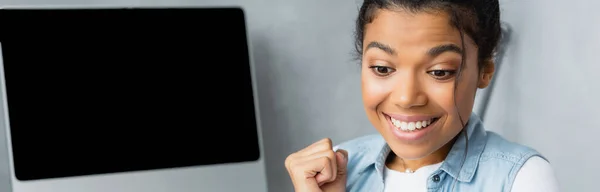 Excited african american freelancer showing winner gesture near monitor with blank screen, banner — Stock Photo